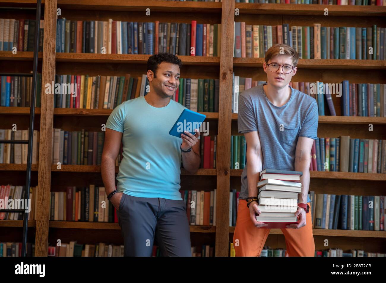 Deux jeunes hommes debout dans la bibliothèque qui tient des livres Banque D'Images