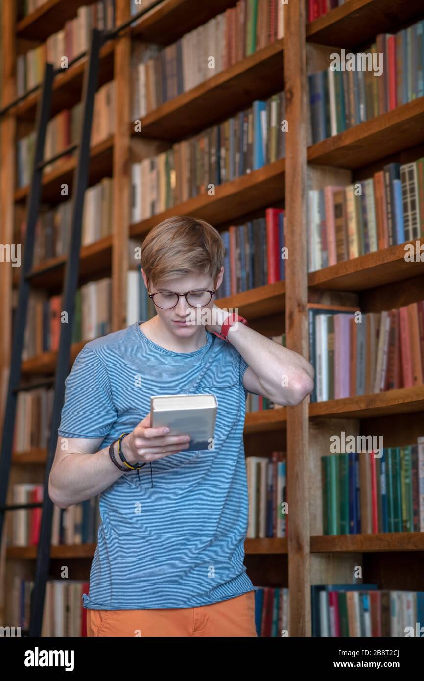 Jeune homme dans les lunettes de lecture d'un livre et regardant intéressé Banque D'Images