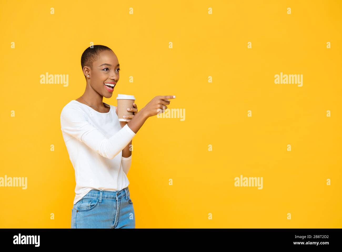 Heureuse belle femme africaine américaine buvant du café souriant et pointant vers l'espace vide à côté isolé sur fond jaune Banque D'Images