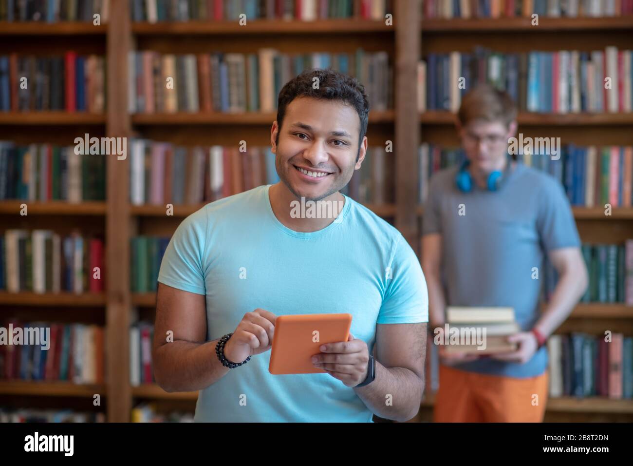 Jeune latino à poil foncé dans un t-shirt bleu portant une tablette Banque D'Images
