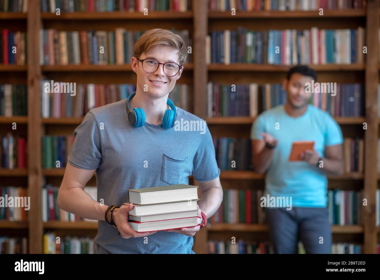 Jeune homme aux cheveux justes dans des lunettes debout dans la bibliothèque avec son ami Banque D'Images