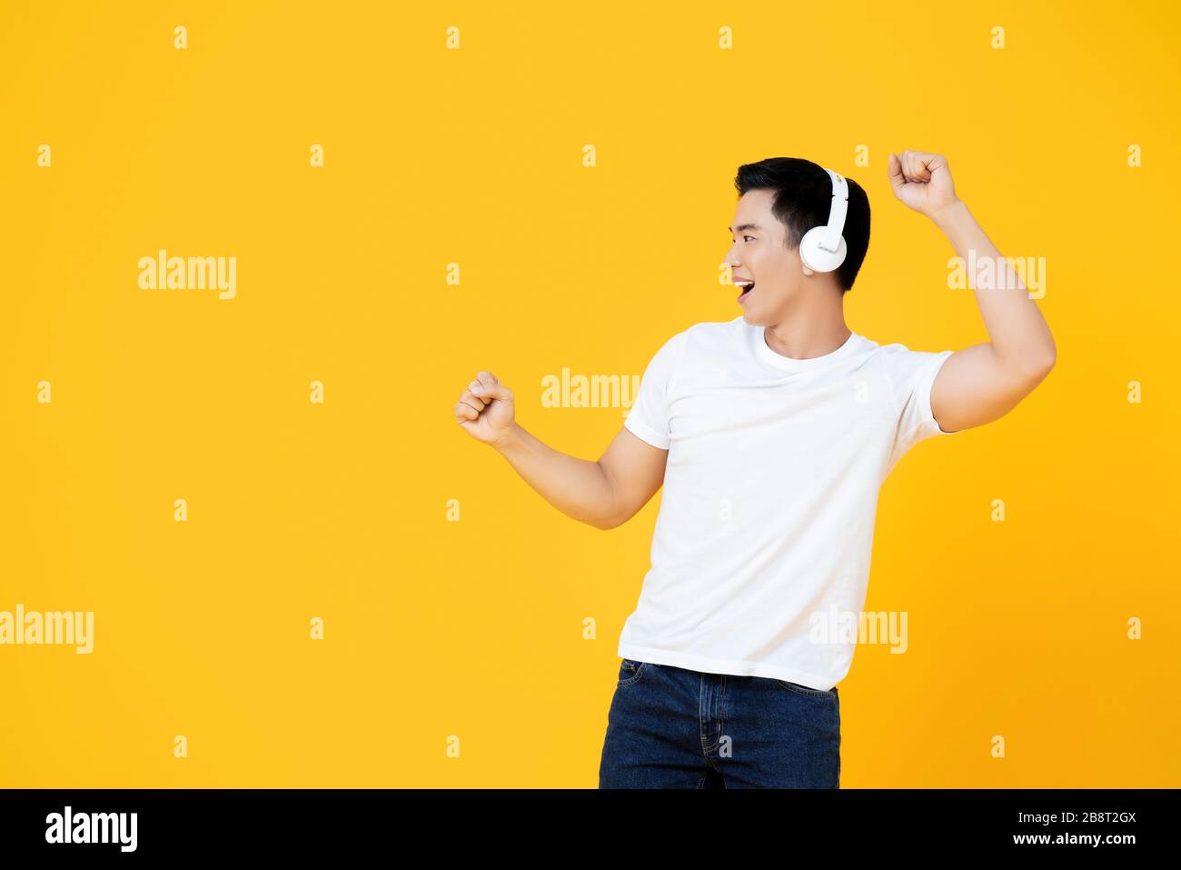Jeune homme asiatique portant des écouteurs écoutant de la musique et dansant sur fond jaune Banque D'Images
