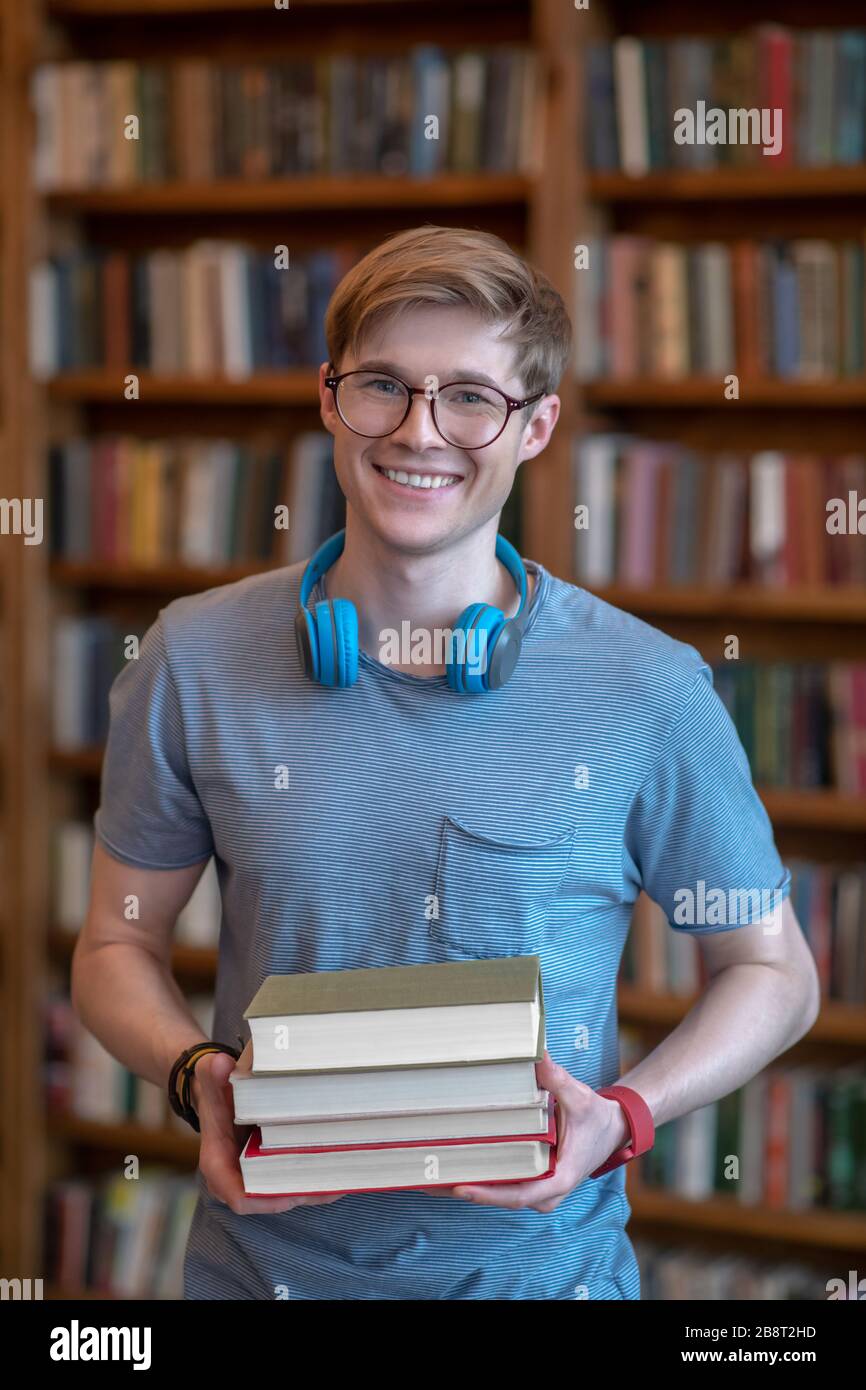 Jeune homme aux cheveux justes dans des lunettes debout dans la bibliothèque et souriant Banque D'Images