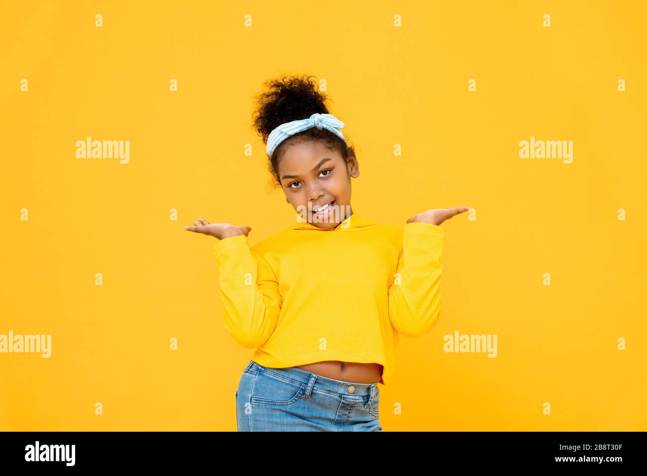 Jeune fille de race mélangée africaine mignonne souriant et faisant des mains ouvertes geste isolé sur fond jaune coloré Banque D'Images