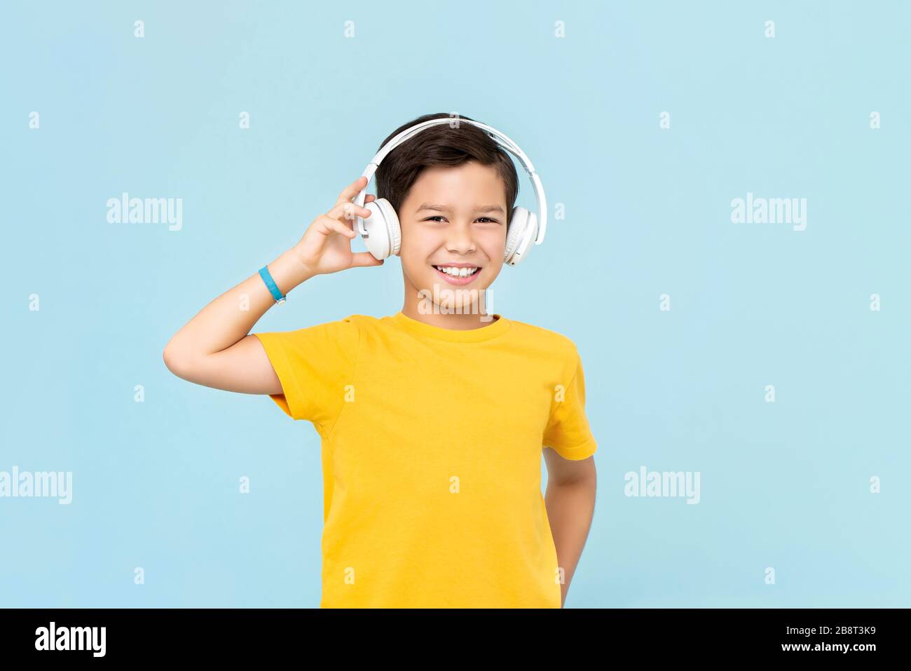 Un jeune garçon souriant et souriant, qui porte un casque sans fil, écoute de la musique isolée sur fond bleu clair Banque D'Images