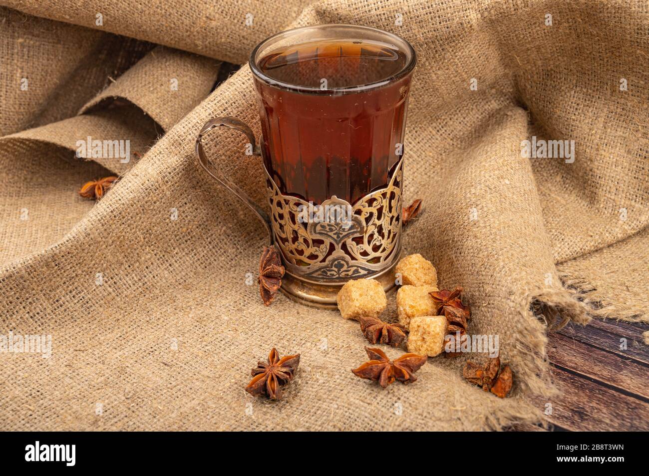 Un verre à facettes de thé dans un porte-gobelet millésime , sucre de canne brun et chocolat sur un fond de tissu à l'homespun grossier. Gros plan Banque D'Images