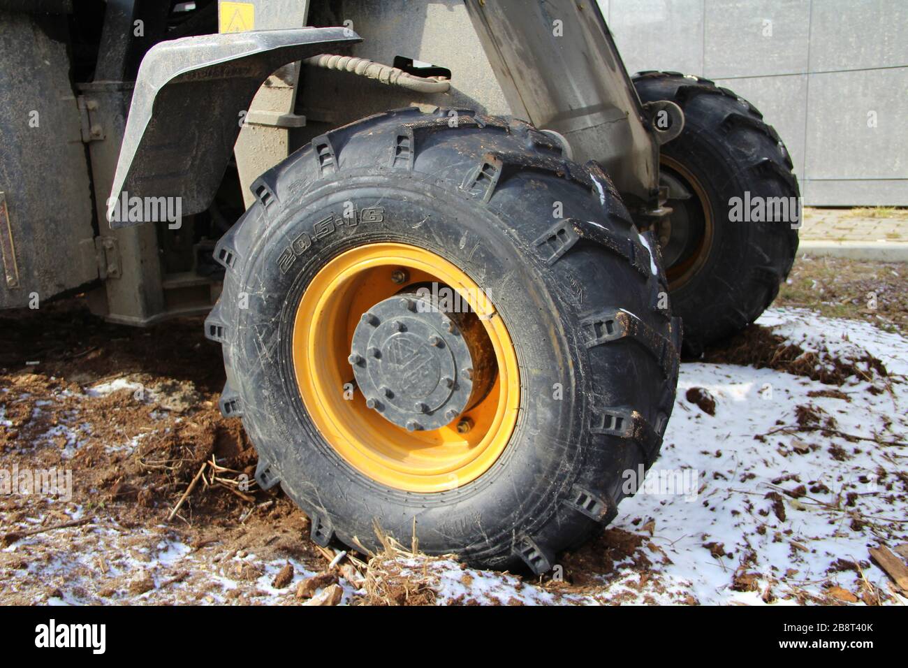 La roue noire et jaune du tracteur avec une bande de roulement puissante sur le pneu se tient sur un sol gelé avec de la neige. Banque D'Images