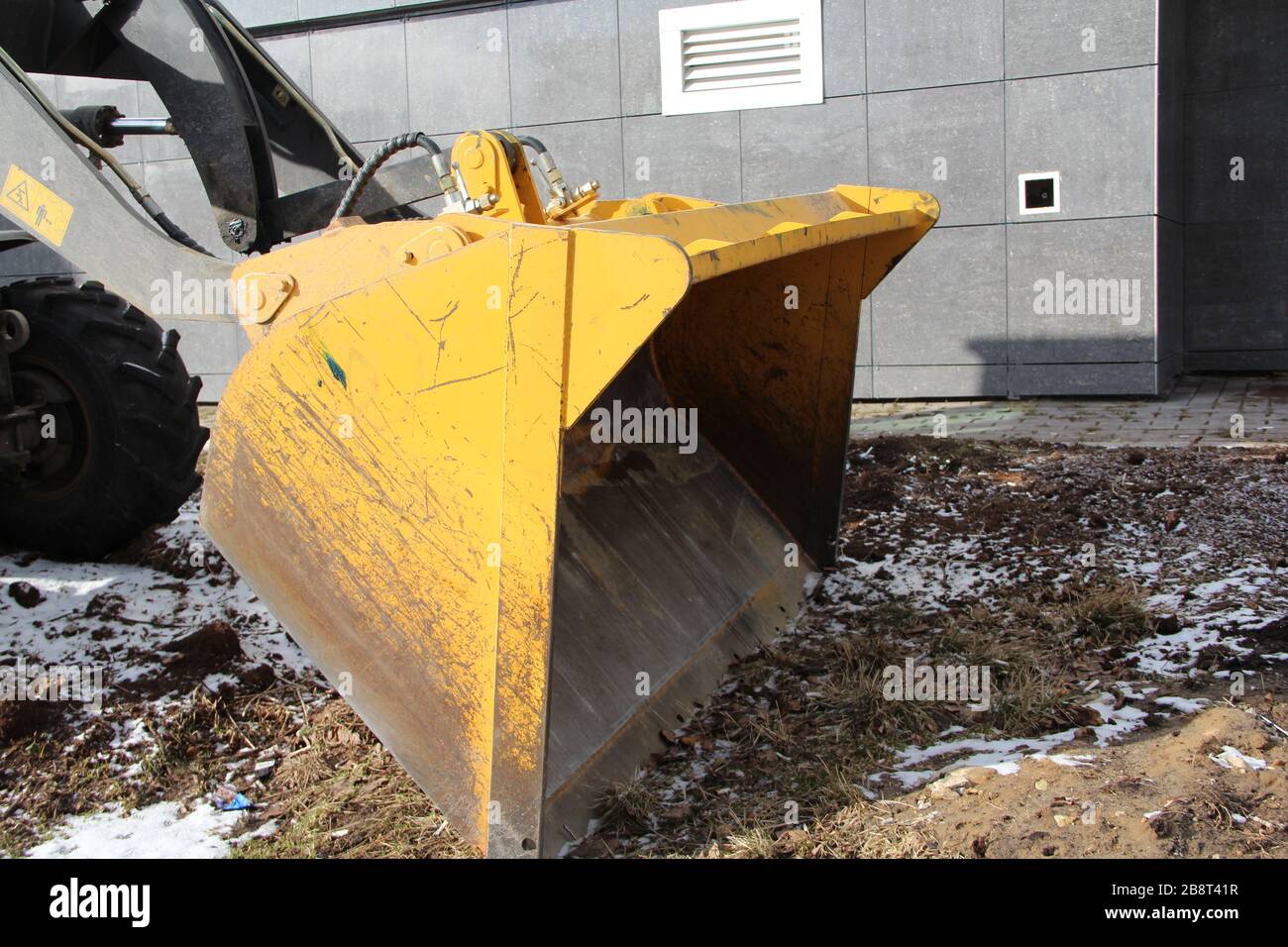 Couteau de tracteur jaune sur le sol contre le fond d'une maison dans la ville. Banque D'Images