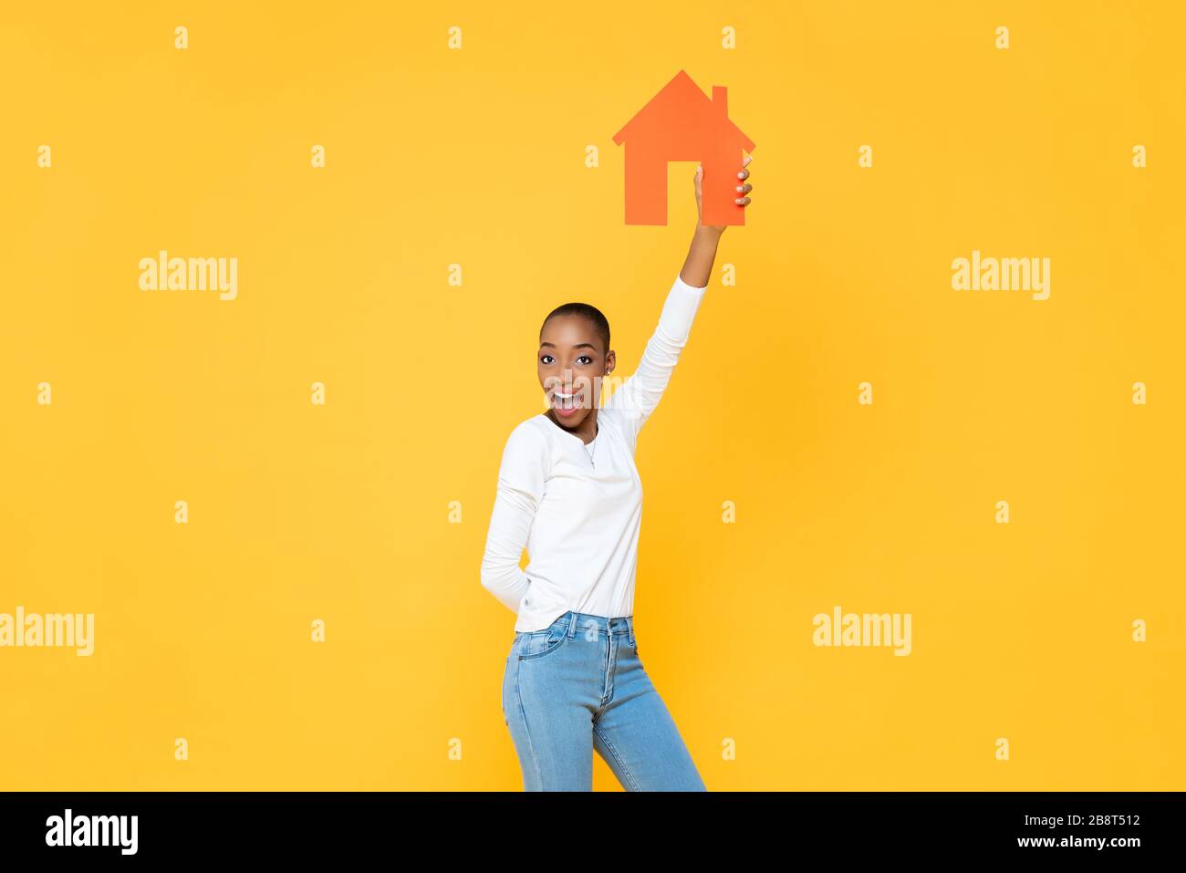 Une femme afro-américaine souriante et confiante tenant l'icône de la maison s'est découpée dans un fond de studio isolé en jaune Banque D'Images