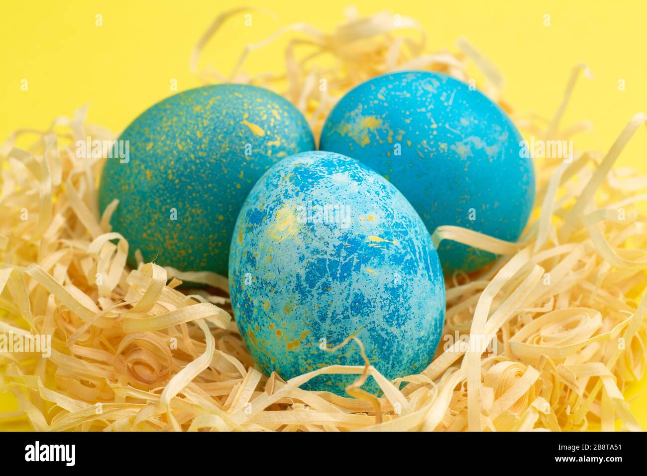 L'oeuf de Pâques peint bleu avec de l'or. L'oeuf se trouve dans un nid de copeaux de bois. Oeuf de pâques peint sur un fond jaune. Gros plan. Banque D'Images