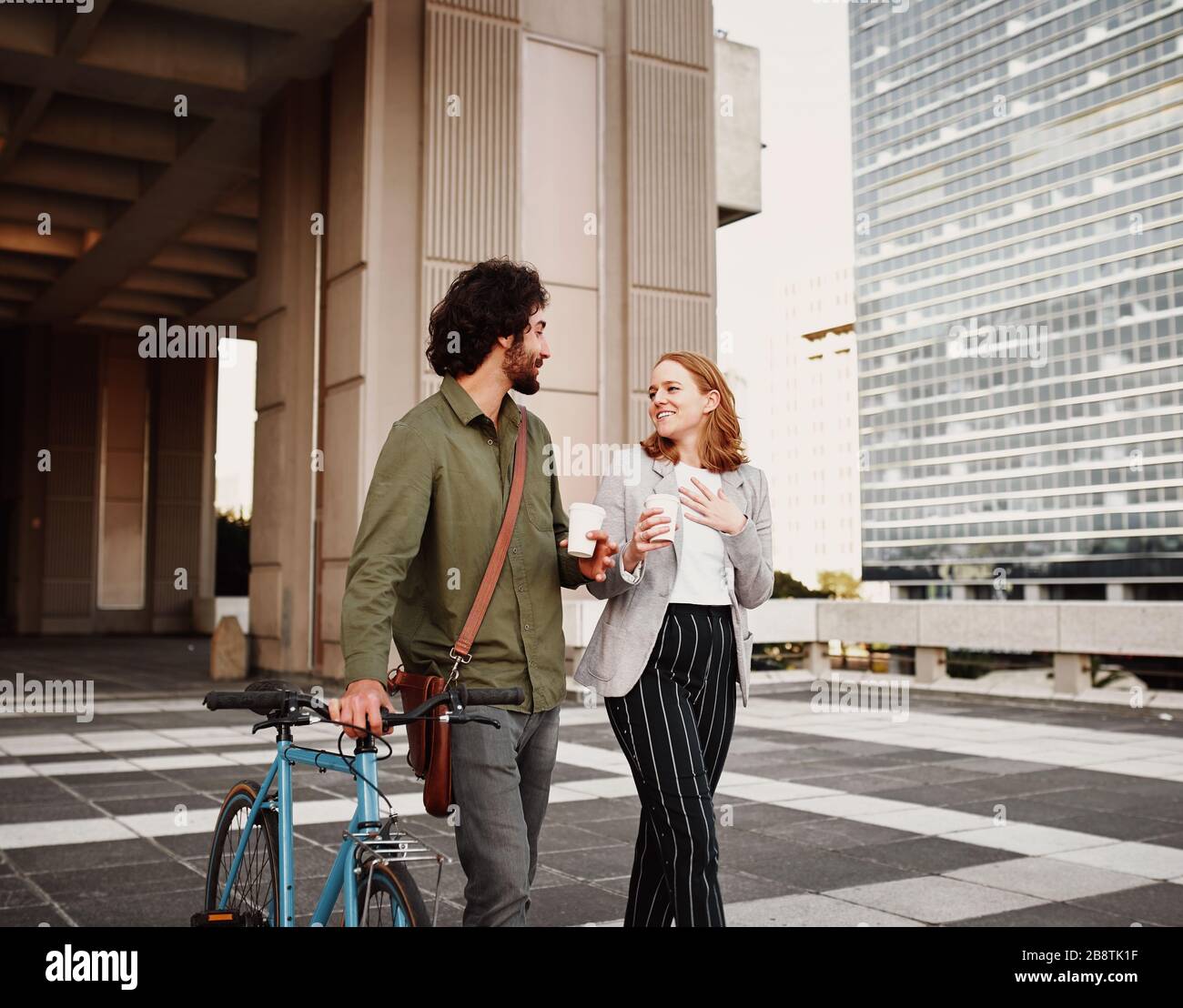 Homme d'affaires avec vélo et sac à bandoulière marchant avec une femme tenant une tasse à café jetable Banque D'Images