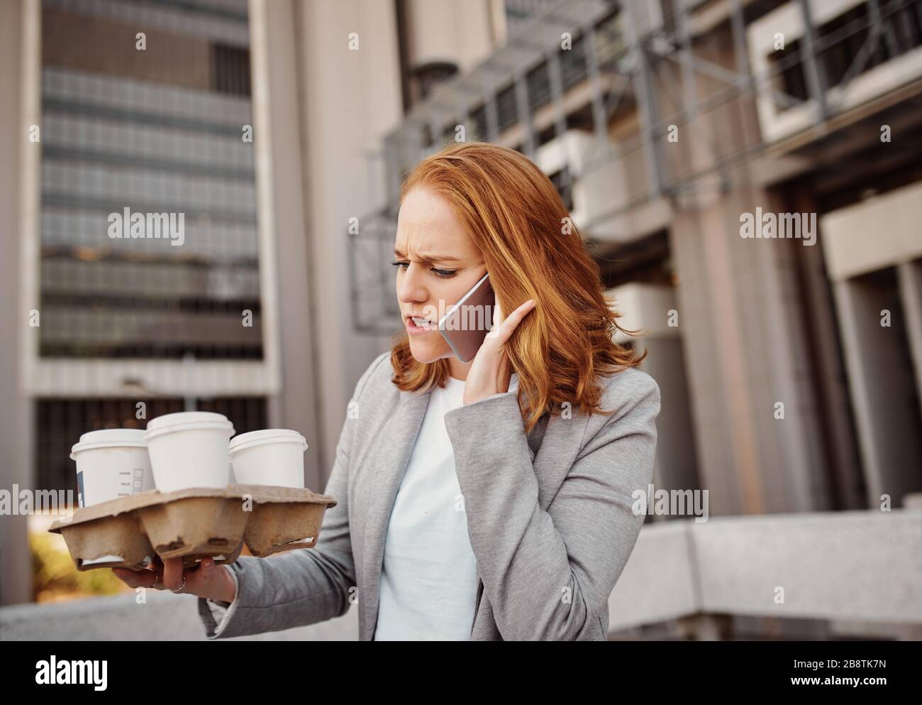 Femme stressée parlant au téléphone portable tenant un plateau de voyage avec des tasses à café jetables Banque D'Images