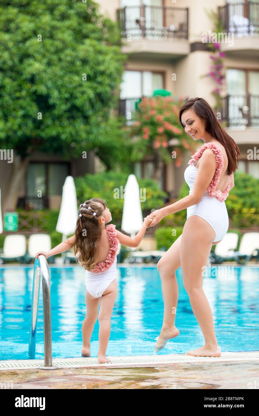 Jeune maman avec bébé fille dans les mêmes maillots de bain blancs sont sur  le bord de la piscine. Vêtements pour l'été et la famille de la mer look  Photo Stock -