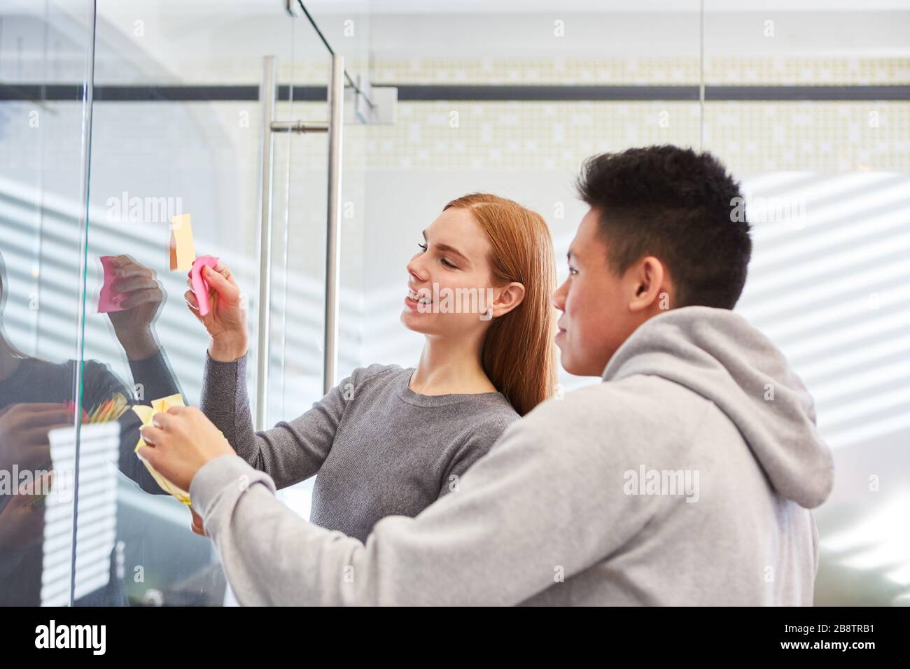 Une femme d'affaires et un collègue remue-méninges avec des notes adhésives sur le mur de verre Banque D'Images