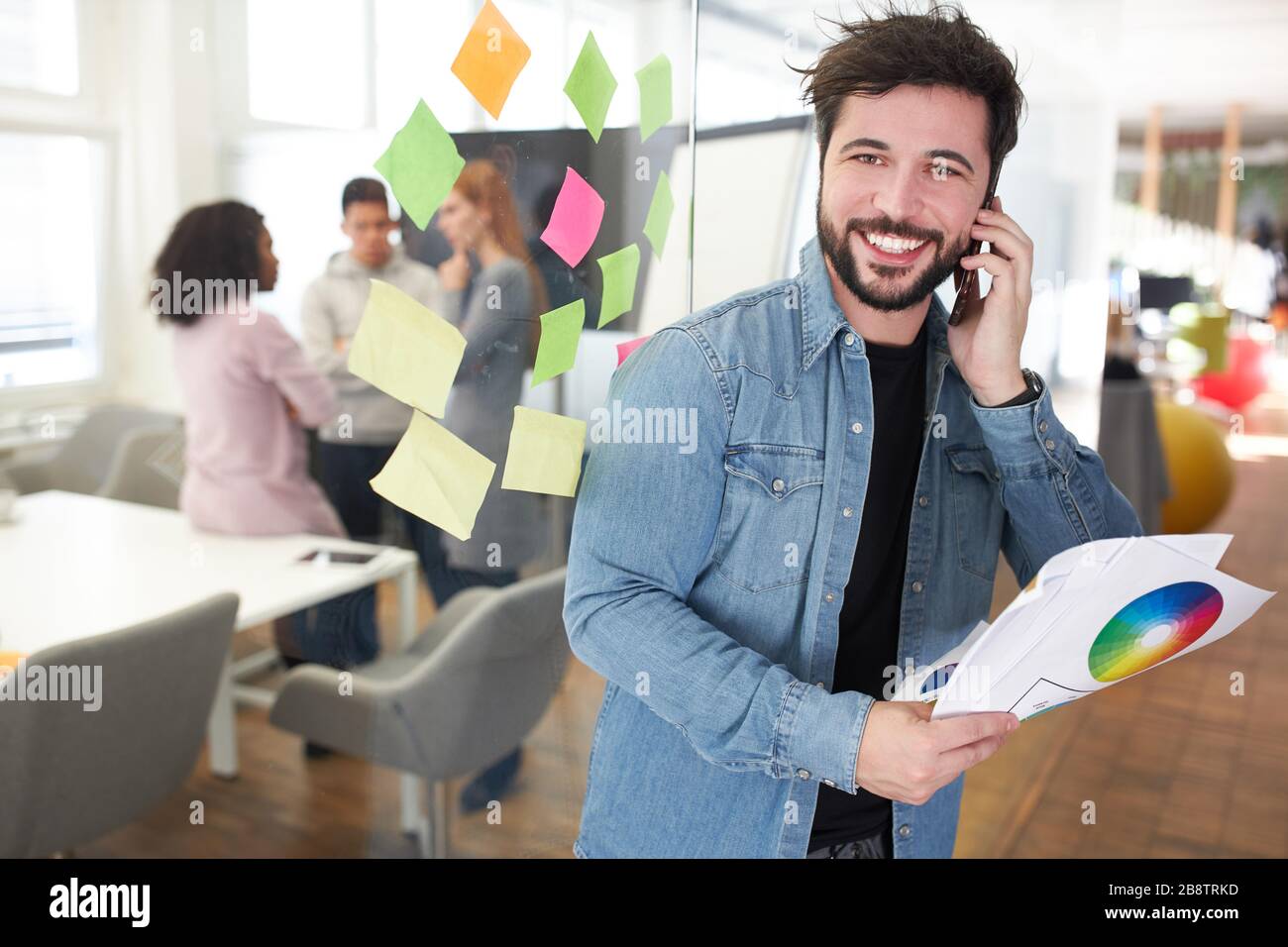 Graphiste comme entrepreneur avec smartphone dans le bureau d'une agence Internet Banque D'Images