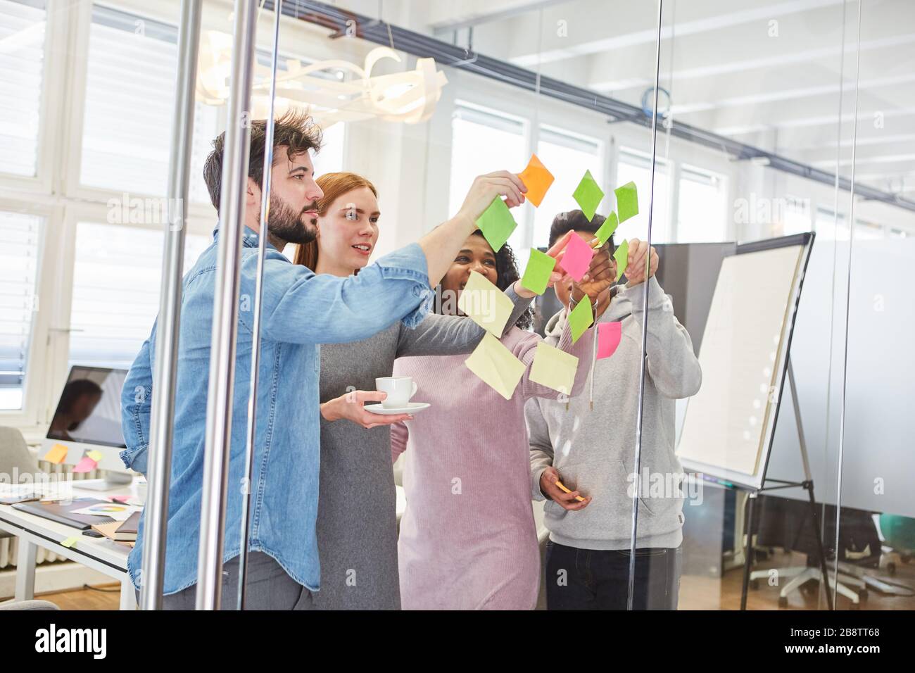 Des étudiants ou une jeune équipe de démarrage dans l'atelier de brainstorming avec des notes sur un mur de verre Banque D'Images
