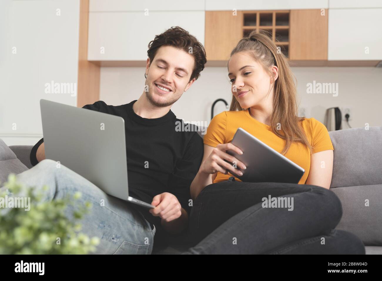 Couple utilisant Internet à domicile rapide avec ordinateur portable et tablette numérique. Femme et homme sur canapé dans le salon Banque D'Images