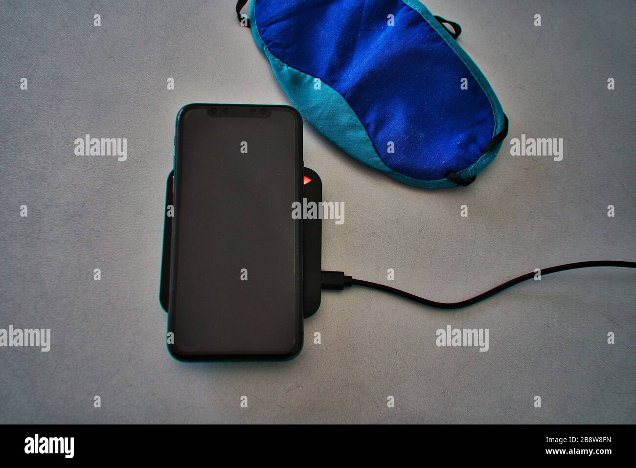 Chargeur sans fil noir de bureau avec voyant de charge pour charger un smartphone. Affichage en noir. Table grise argent. Masque de nuit bleu sur la table Banque D'Images