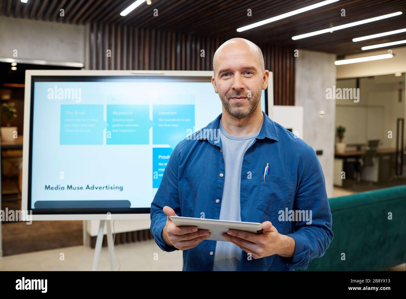 Taille vers le haut portrait de l'homme adulte chauve souriant à l'appareil photo et tenant la tablette tout en se tenant contre la carte numérique pendant la présentation marketing, copier spac Banque D'Images