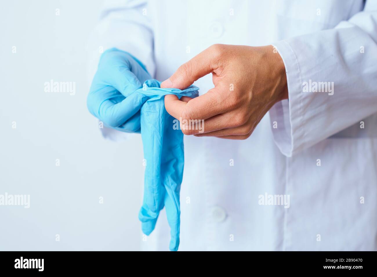 closeupo d'un homme de docteur caucasien, portant un manteau blanc, mettant sur une paire de gants chirurgicaux bleus Banque D'Images