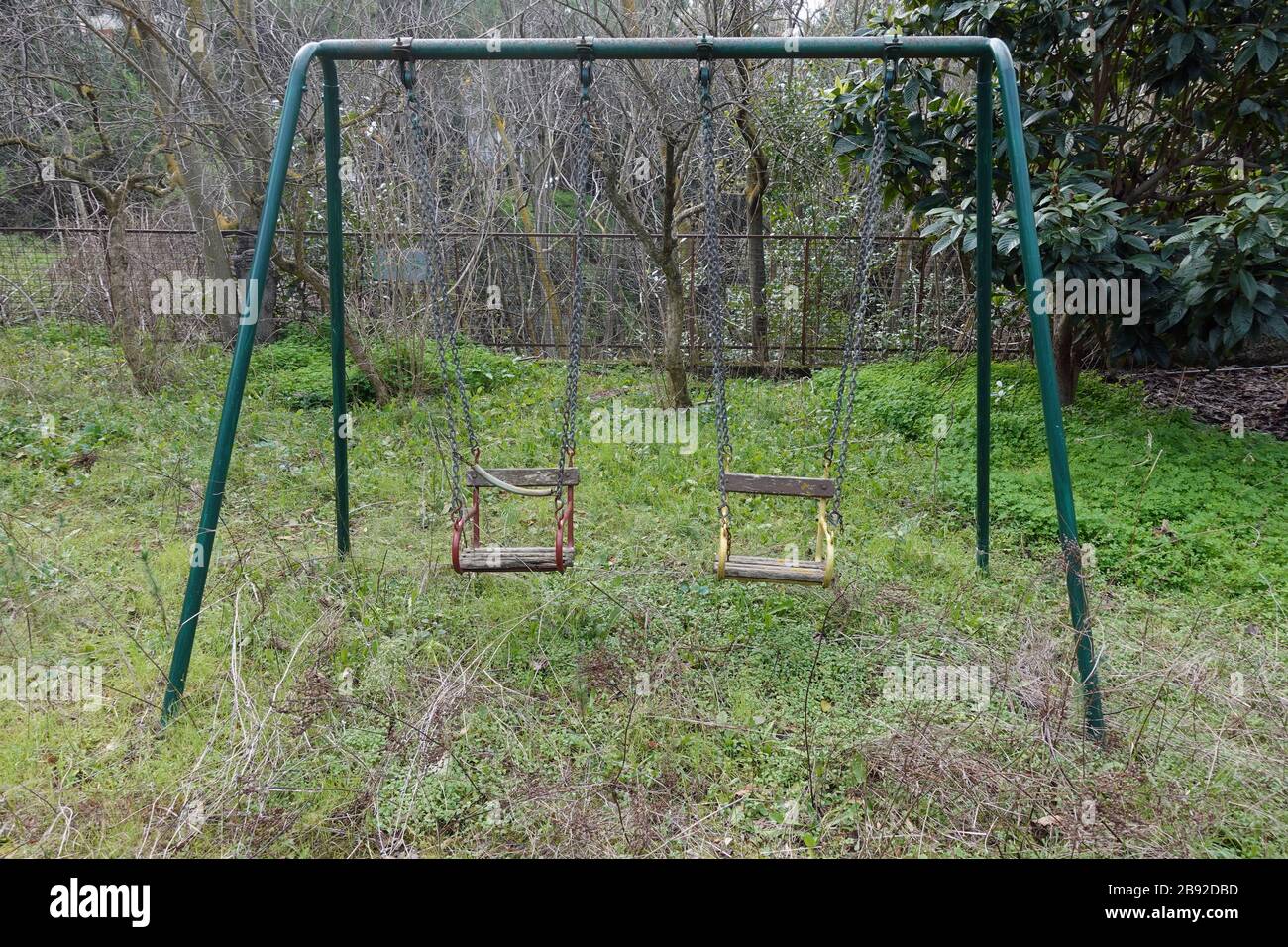 Balançoires rouillées dans le terrain de jeux pour enfants abandonné en surculture. Banque D'Images