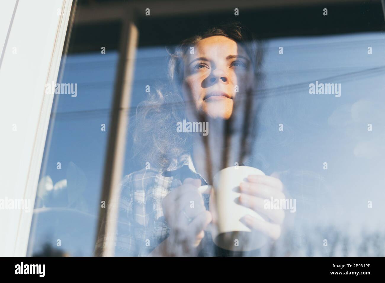 Jeune femme blonde regardant hors de la fenêtre avec une expression concernée sur son visage. Réflexion dans le verre, effet de double exposition Banque D'Images