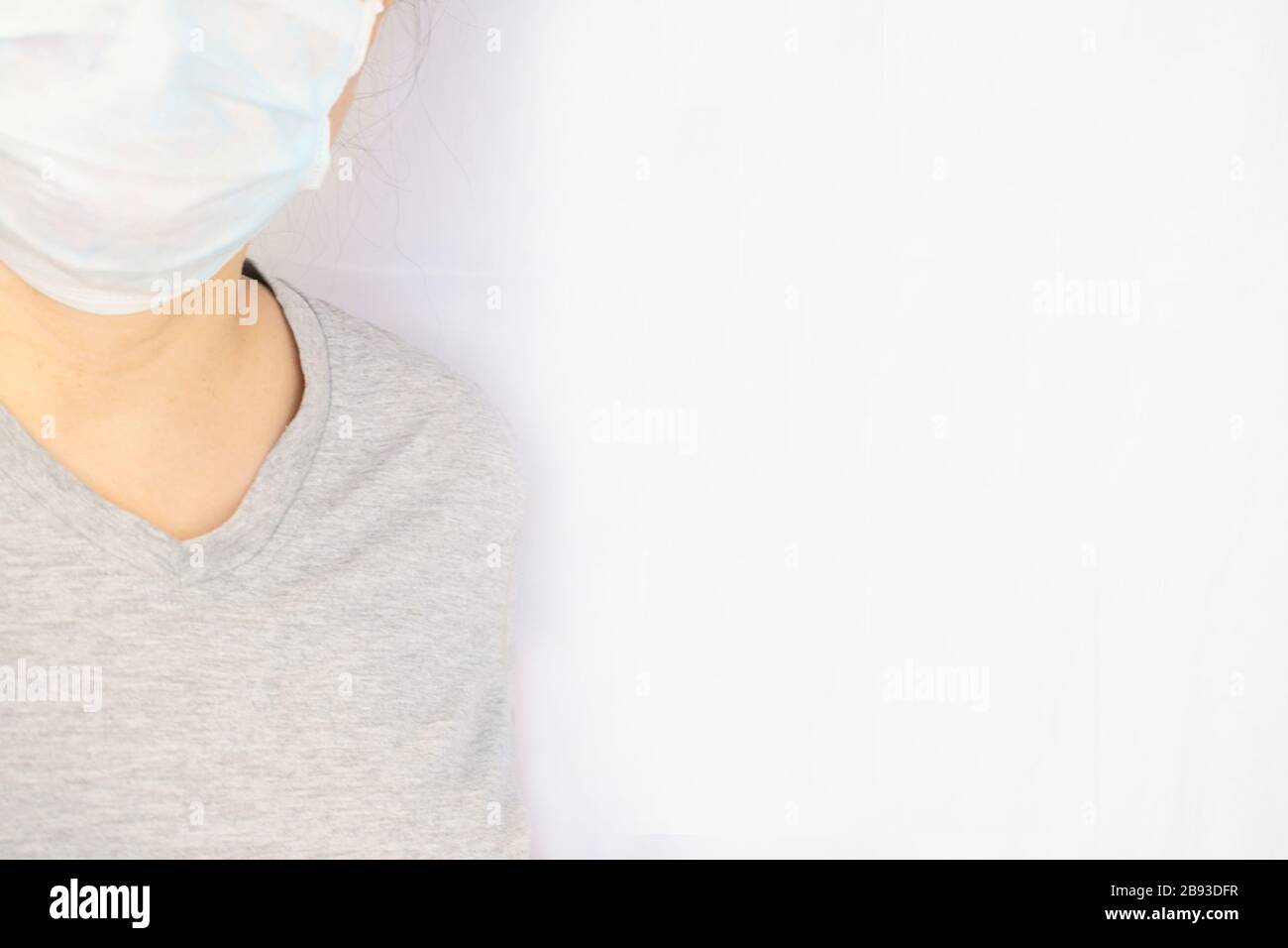 Femme portant un masque facial lors de la nouvelle pandémie de coronavirus, alias Covid-19. Portrait candié, visage partiel et corps avec un fond draperie blanc pour la cdp Banque D'Images