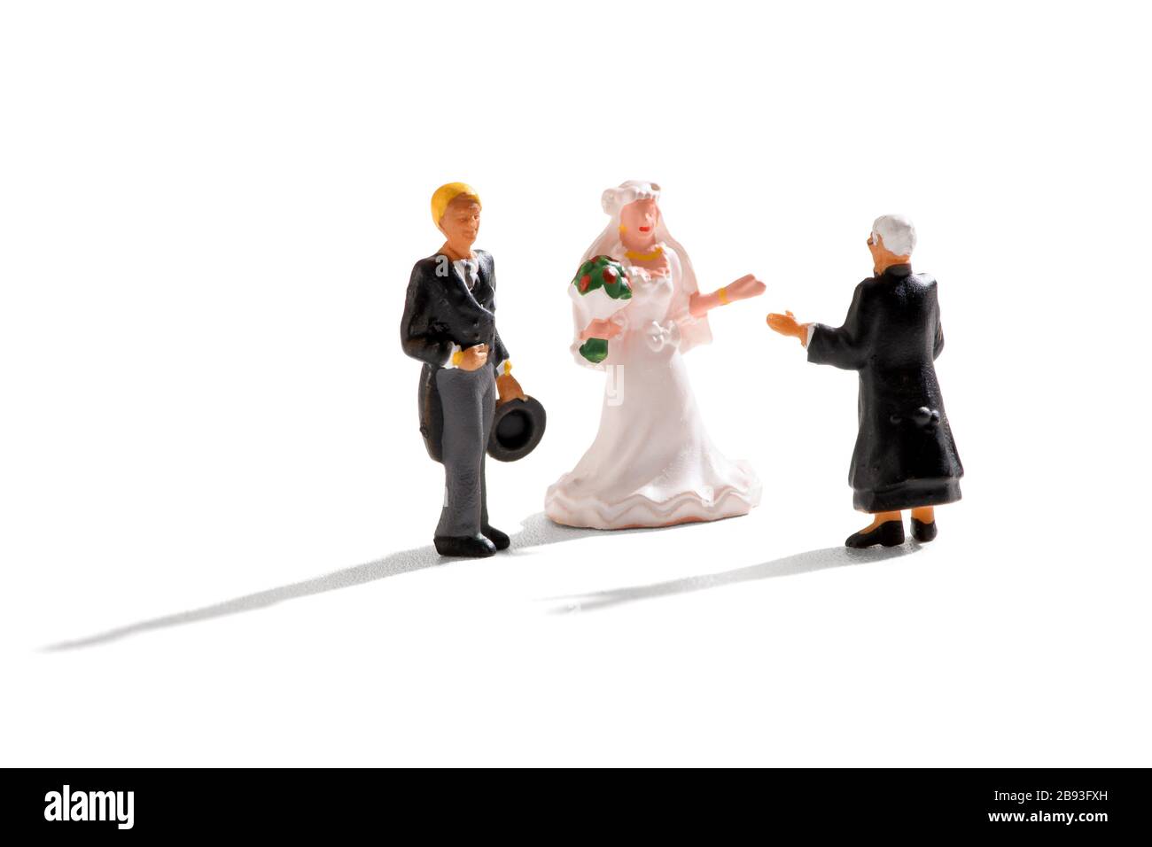 Prêtre menant une scène de mariage miniature avec marié et épouse dans une robe blanche sur un fond blanc avec des ombres Banque D'Images