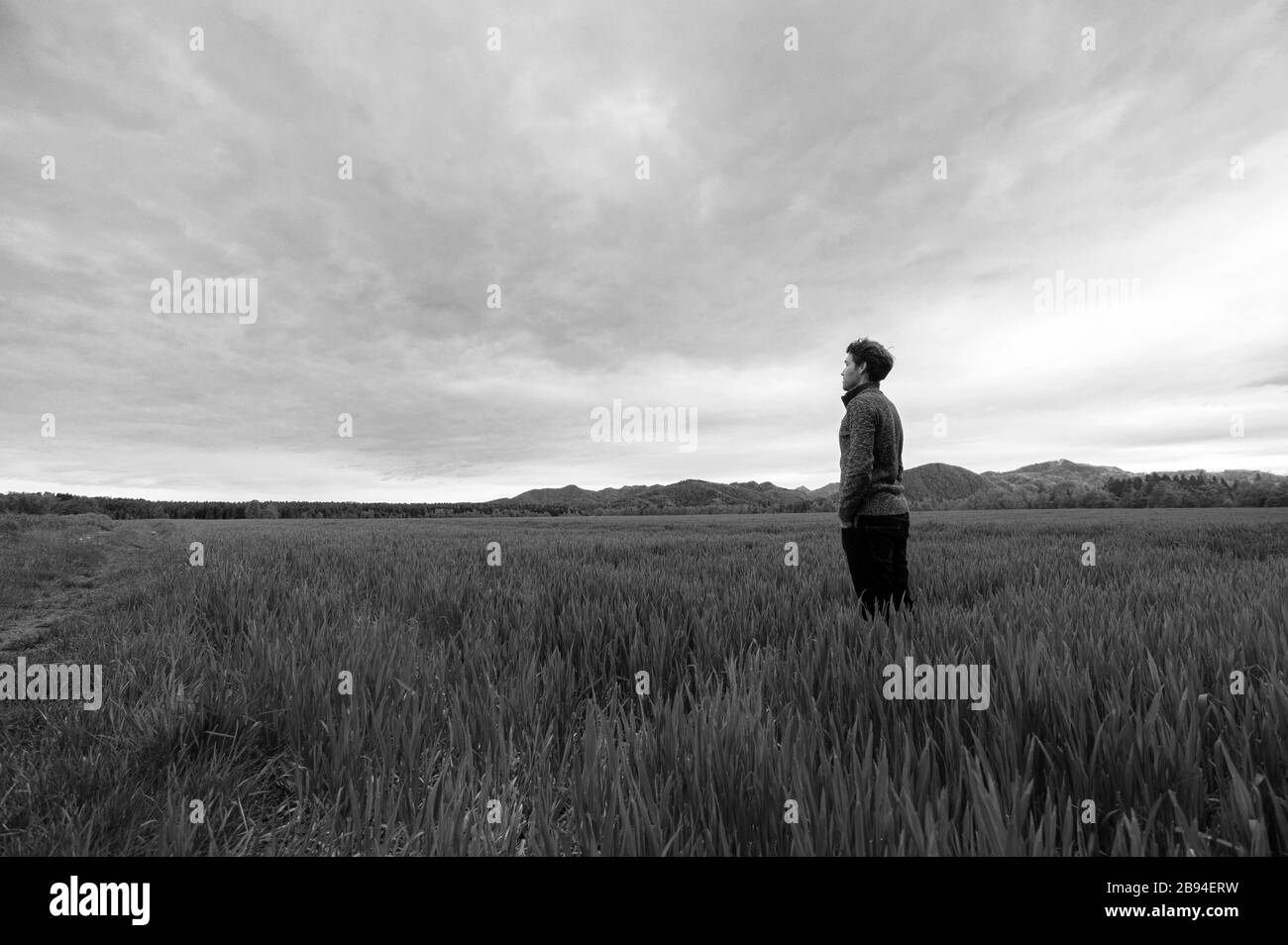 Image monochrome d'un jeune homme debout dans un grand pré sous ciel nuageux majestueux. Banque D'Images