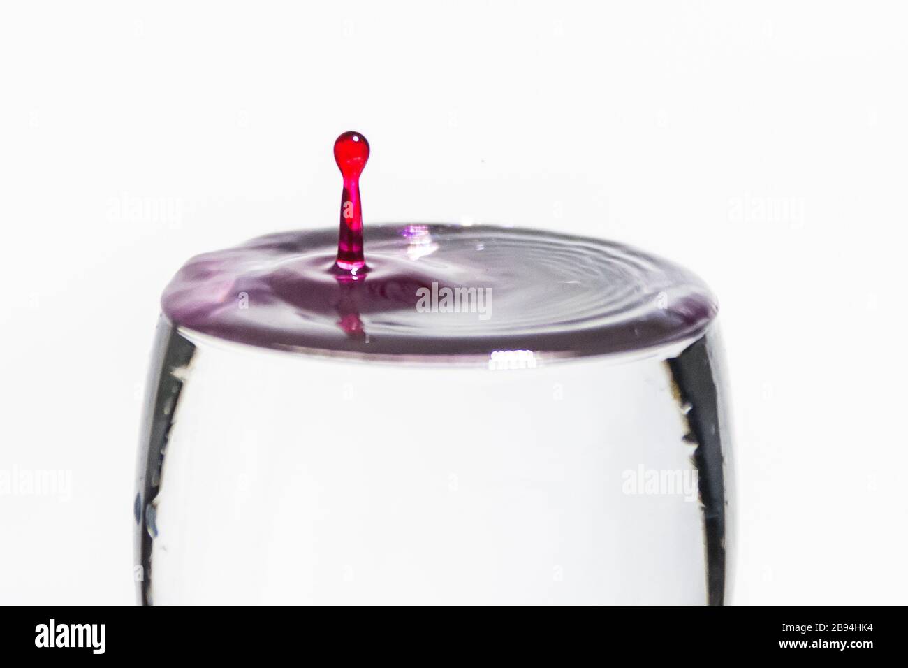 Goutte rouge éclaboussant dans un verre d'eau transparent Banque D'Images