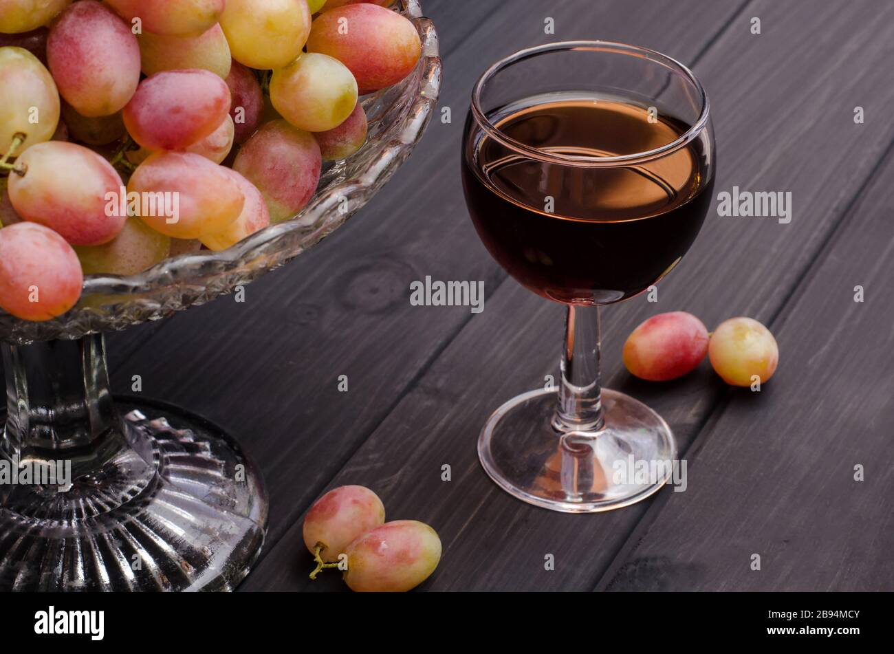 Vin rouge dans un verre avec des raisins dans un vase sur fond en bois noir. Pour la publicité du vin, la vie encore. Banque D'Images