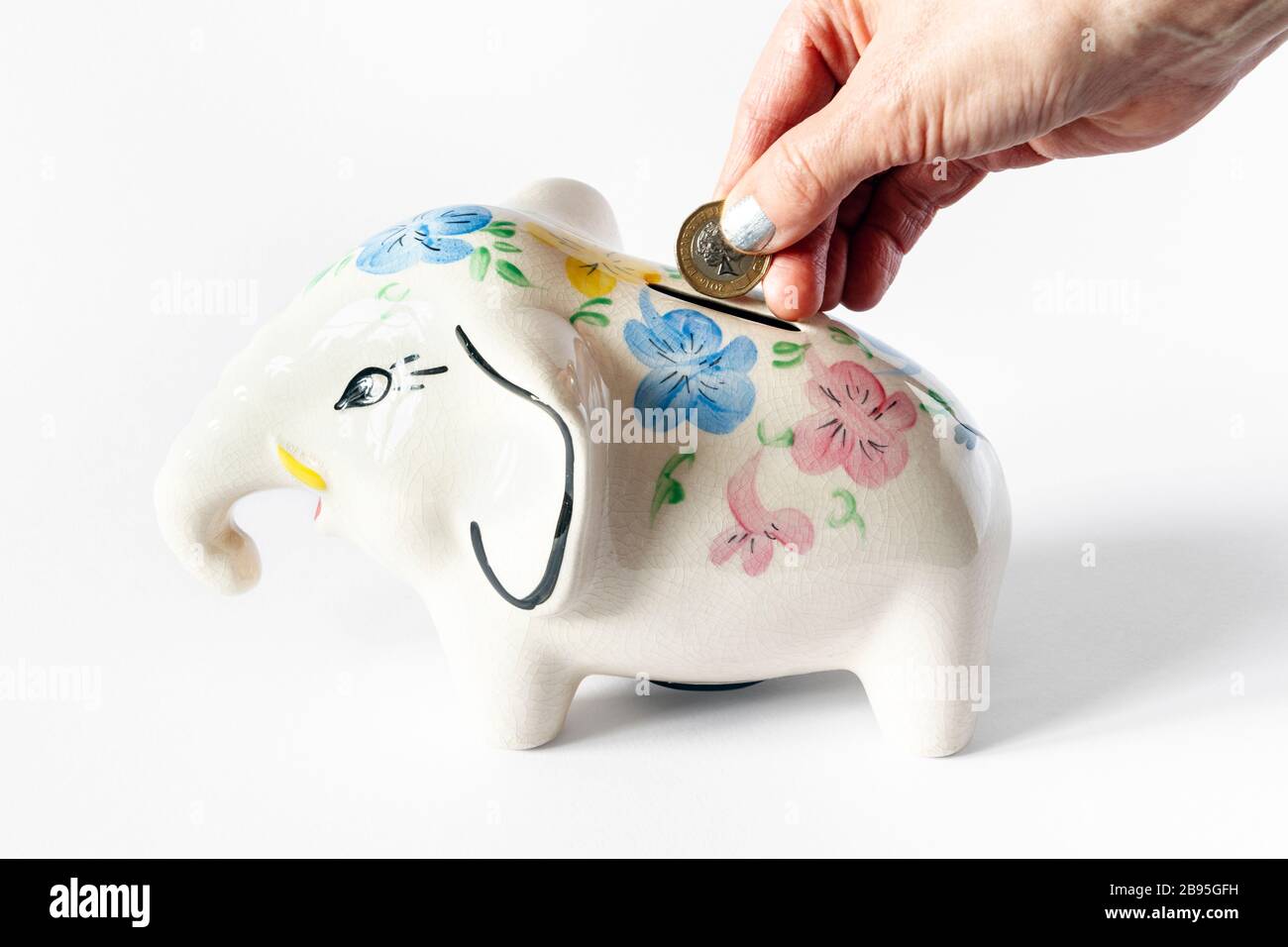 Main femelle avec vernis à ongles argenté insérant une pièce de monnaie en livre dans une boîte d'argent en céramique éléphant Banque D'Images