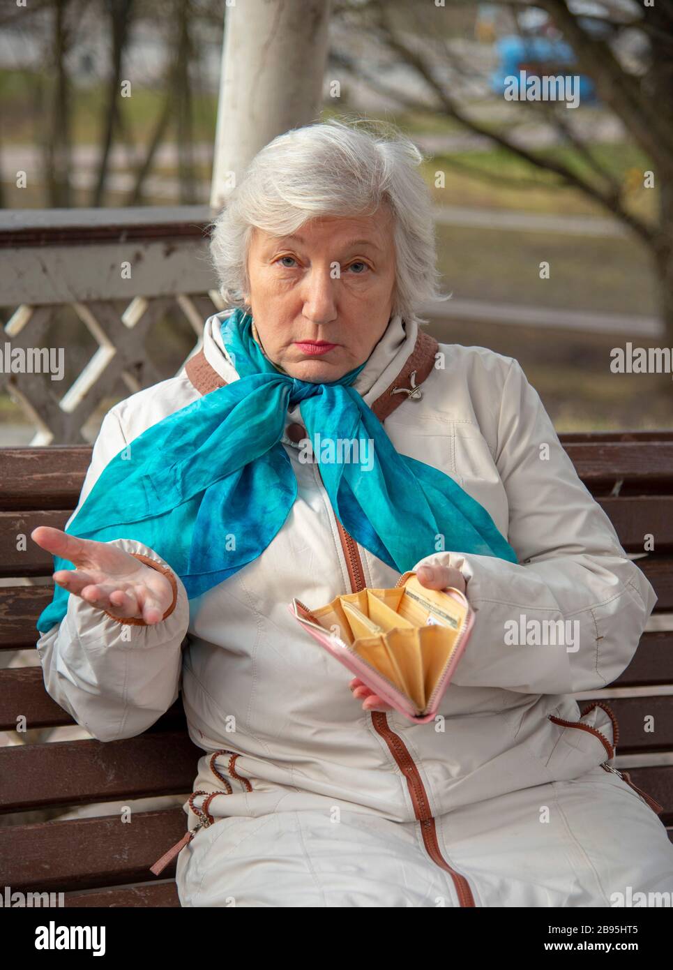 Une femme âgée, triste, habillée avec élégance, est assise sur un banc de parc avec un sac à main vide dans ses mains Banque D'Images