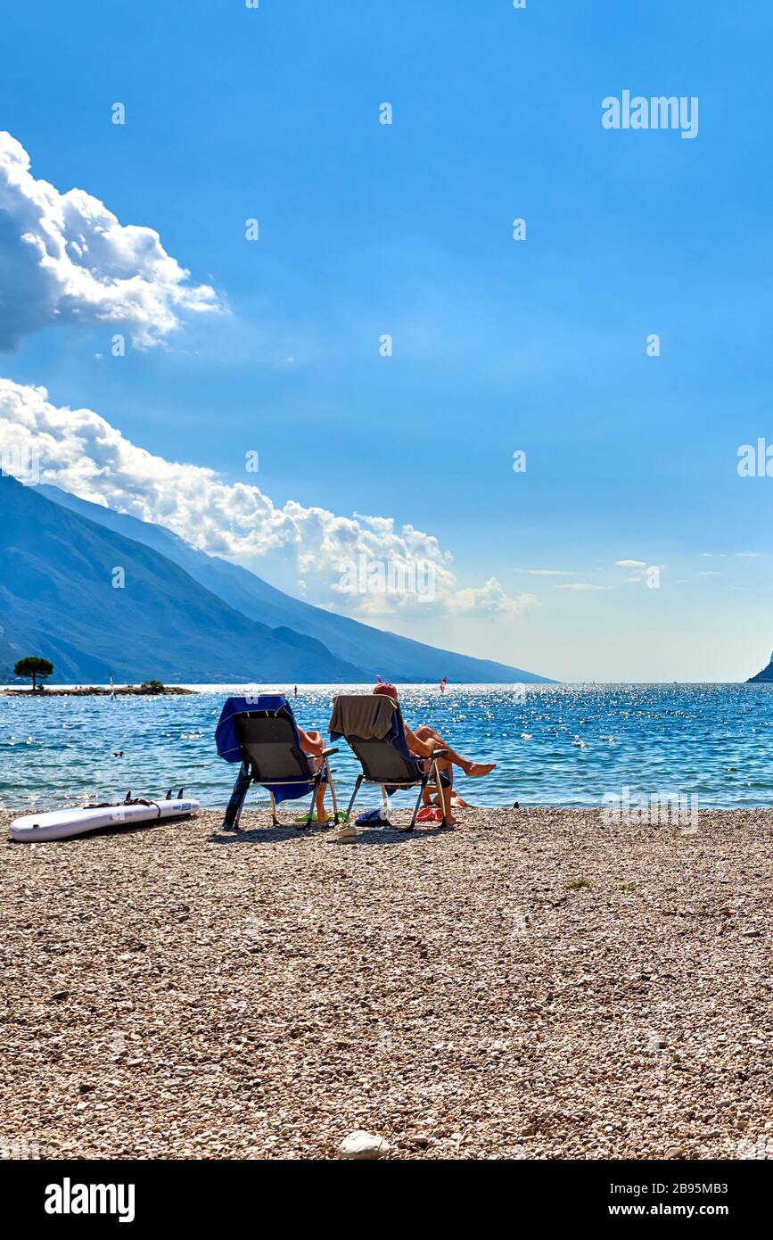 Torbole, Italie-09 octobre 2018 : personnes assises à la plage sur la chaise longue et admirant le lac de Garde en été, vue sur le magnifique lac Banque D'Images