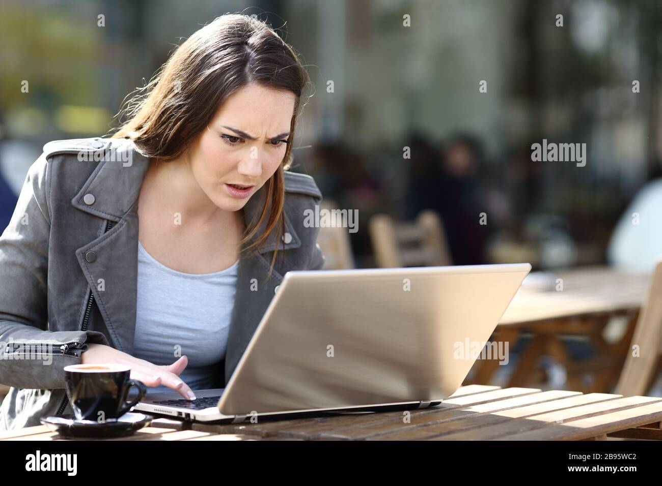 Une femme en colère appuie sur un bouton désespérée vérifier l'ordinateur portable dans une terrasse de café Banque D'Images