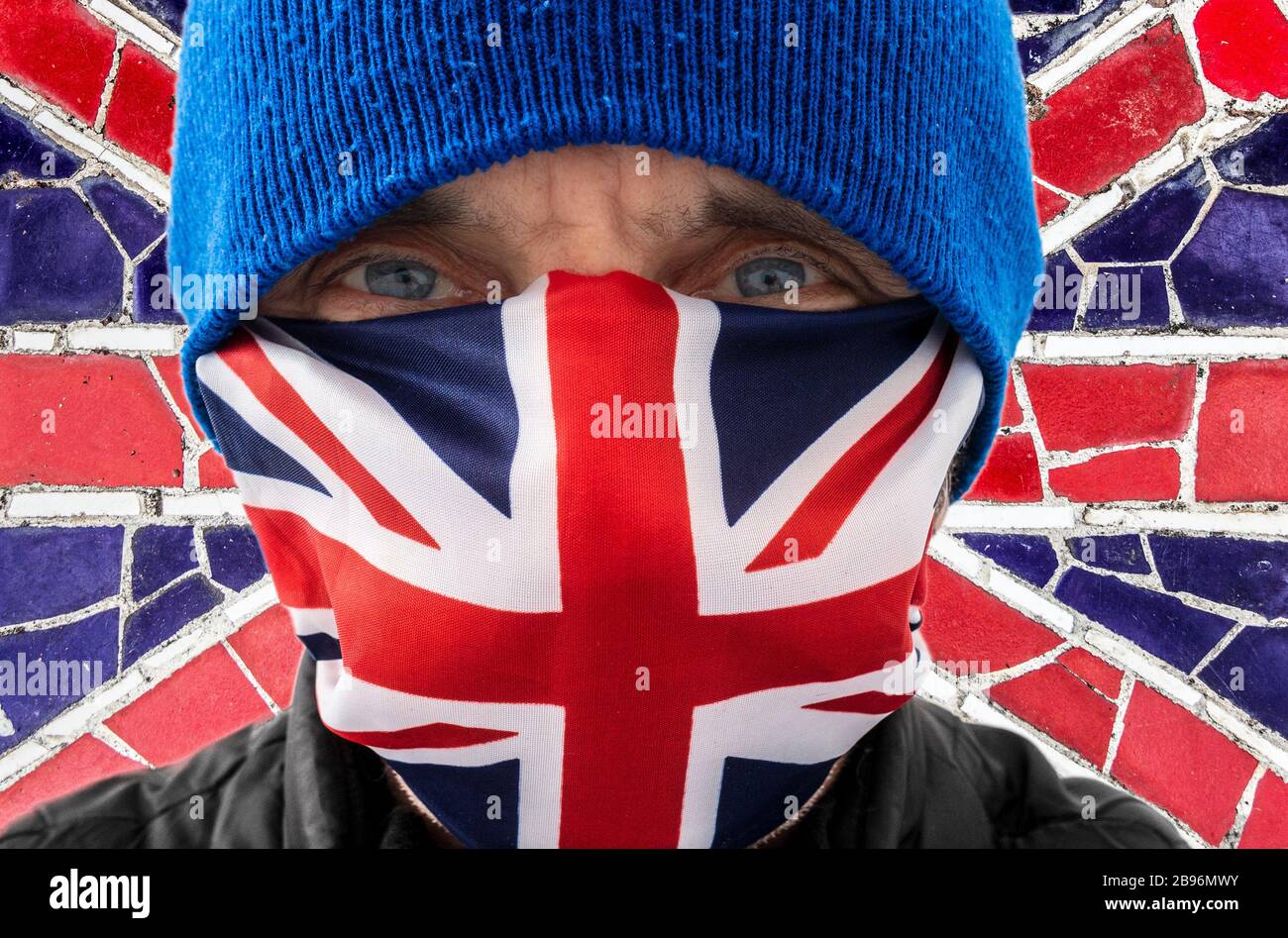 Homme portant le masque de visage de drapeau Union Jackj/Union avec le fond de drapeau britannique. Concept de coronavirus. Banque D'Images