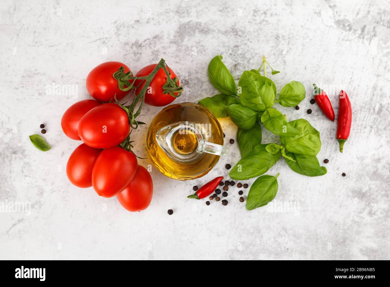 Tomates fraîches colorées, basilic et huile d'olive sur table blanche. Vue de dessus avec espace de copie Banque D'Images