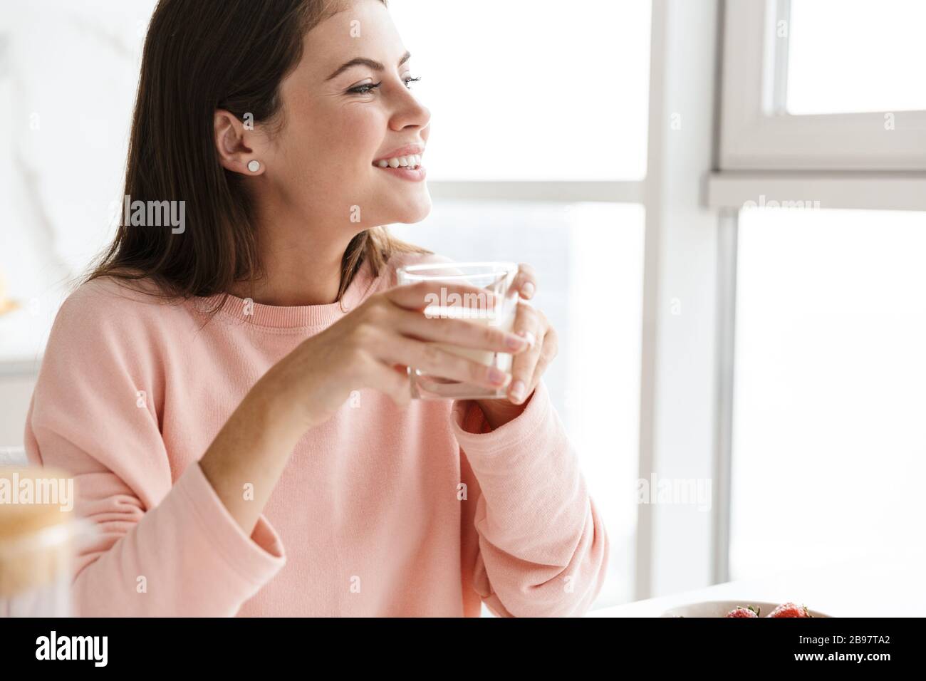 Gros plan sur une jeune fille souriante avec un délicieux petit déjeuner sain tout en étant assise à la table de cuisine, boire du lait Banque D'Images