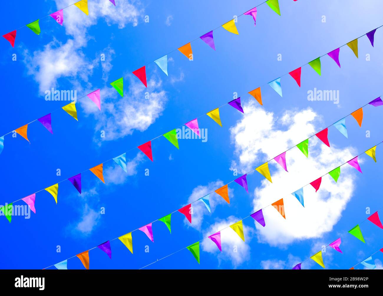 Drapeaux colorés dans le ciel bleu vif avec fond de nuages, festivités d'été, couleurs de l'arc-en-ciel. Banque D'Images