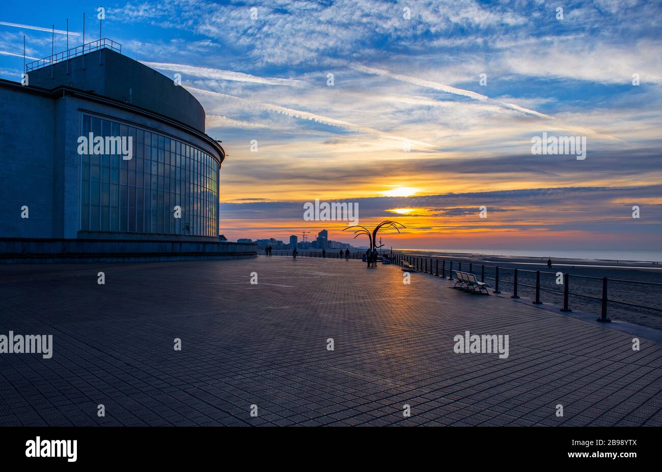 La promenade du bord de mer d'Ostende (Ostende en anglais) au coucher du soleil avec des personnes imreconnaissables silhouette marchant près de la plage, mer du Nord, Belgique. Banque D'Images
