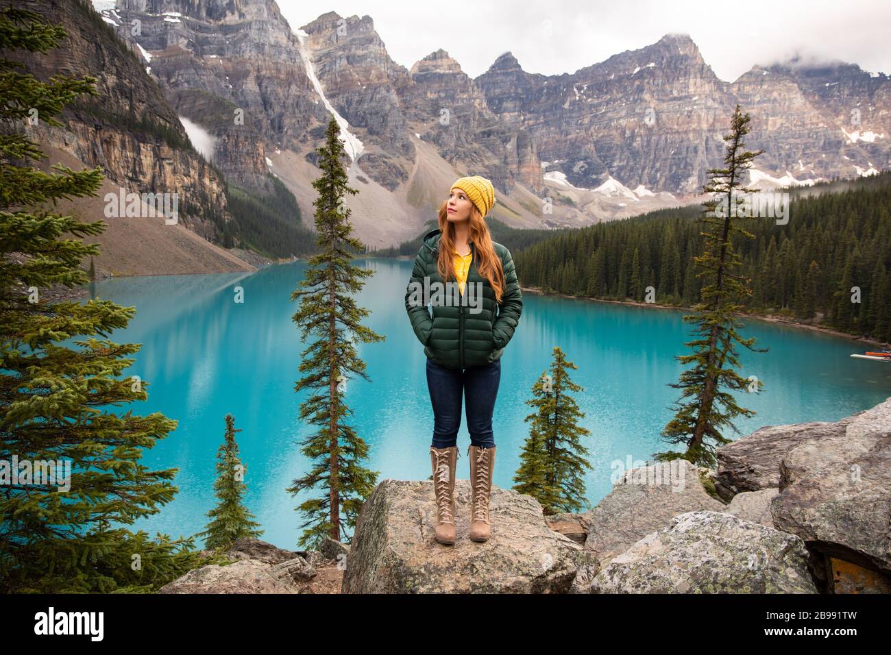 une fille aux cheveux rouges dans un bonnet jaune et des bottes avec lac moraine banff en arrière-plan Banque D'Images