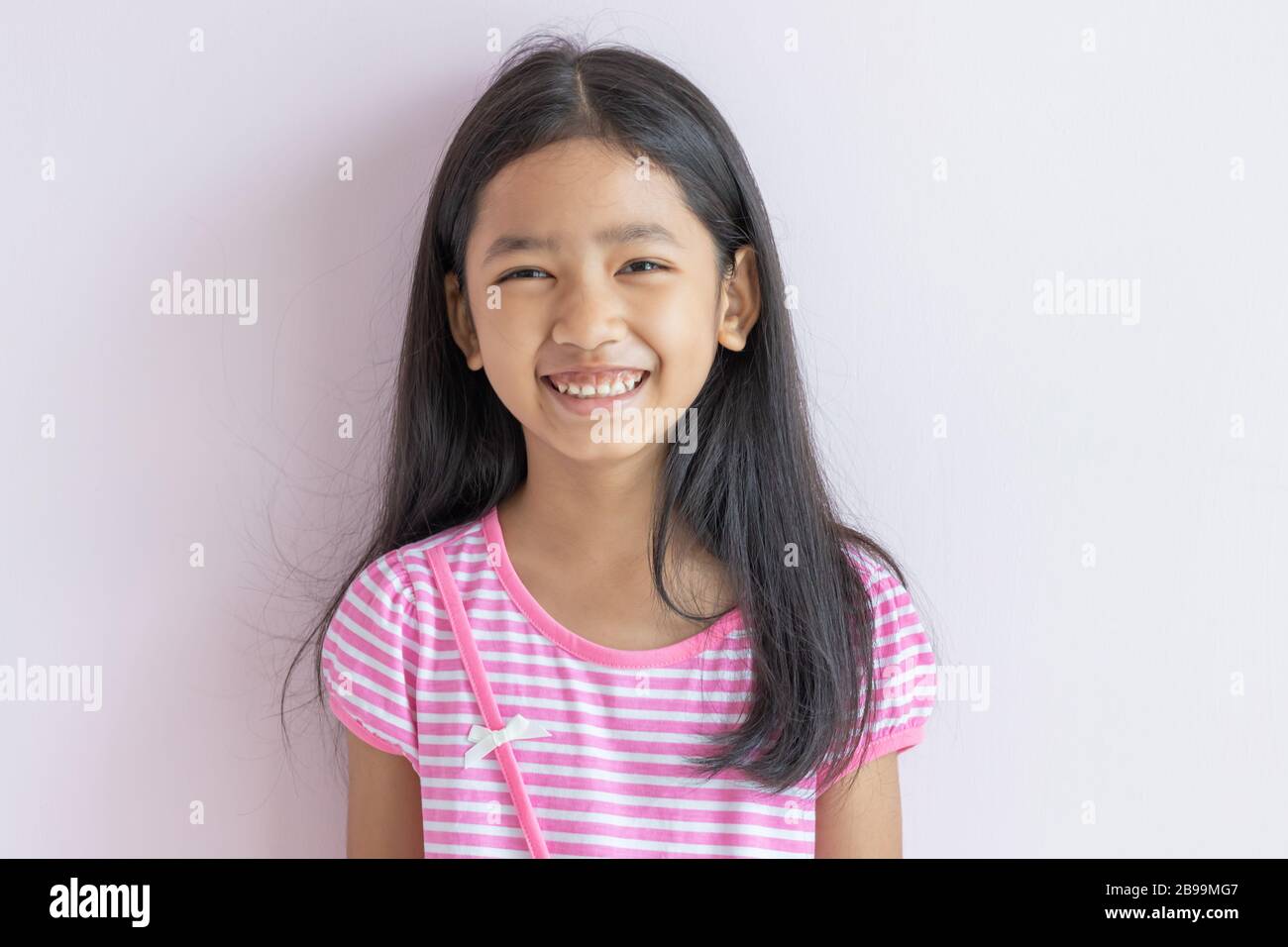 Petite fille asiatique souriante aux couleurs vives. Les enfants portent des robes blanches croisées roses et de longs cheveux noirs. L'enfant regarde vers l'avant et sourit avec plaisir. Portraits Banque D'Images