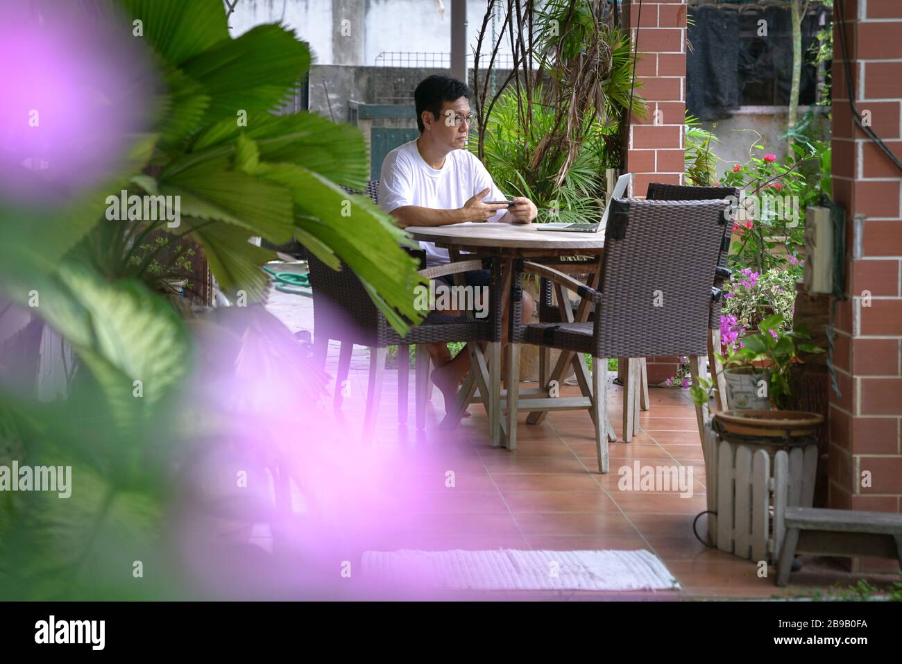 Homme assis à sa maison patio avec vue sur le jardin, travaillant sur son ordinateur. Concept de travail à domicile. Banque D'Images