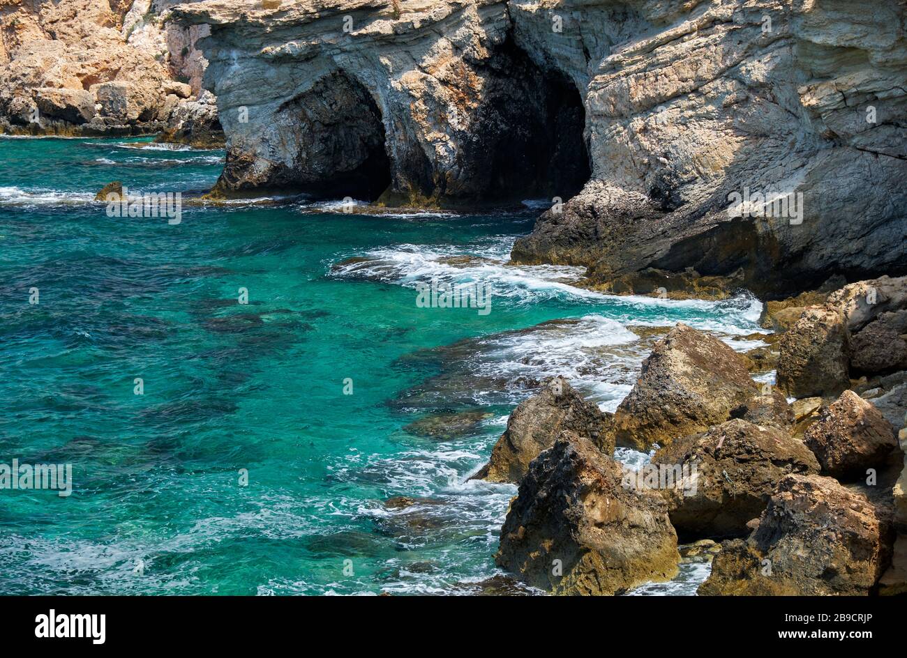 La vue des grottes dans la rive rocheuse surélevée au-dessus de l'eau bleue cristalline du Cap Greco. Chypre Banque D'Images