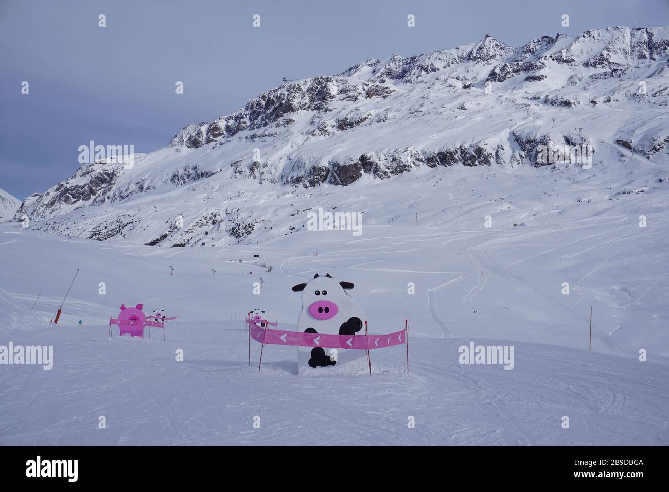 Vache noire et blanche et sculptures de cochon rose sur les pentes d'Alpe d'Huez, France, lors d'une journée hivernale ensoleillée Banque D'Images