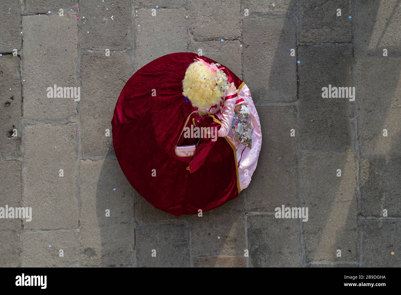 Robe de salle de bal vénitienne en velours rouge vif recouverte de confettis, vue d'en haut, sur la toile de fond de la vieille rue pavée Banque D'Images