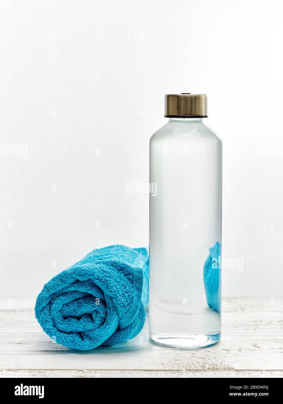 Bouteille d'eau potable en verre réutilisable sur table en bois blanc avec serviette bleue Banque D'Images