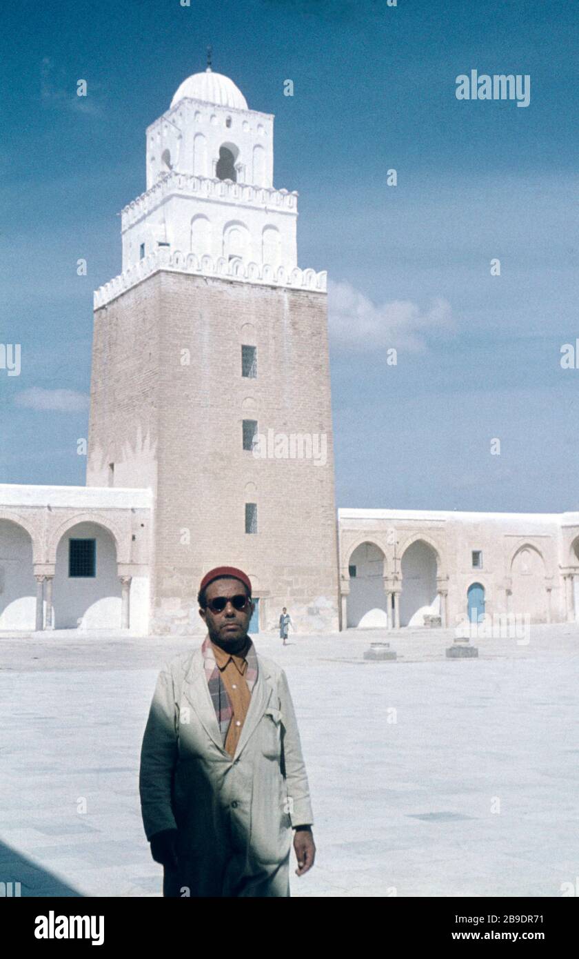 Un homme avec des lunettes de soleil pose pour une photo devant la Mosquée  centrale de Kairouan, en Tunisie. En arrière-plan le minaret de la mosquée.  [traduction automatique] Photo Stock - Alamy