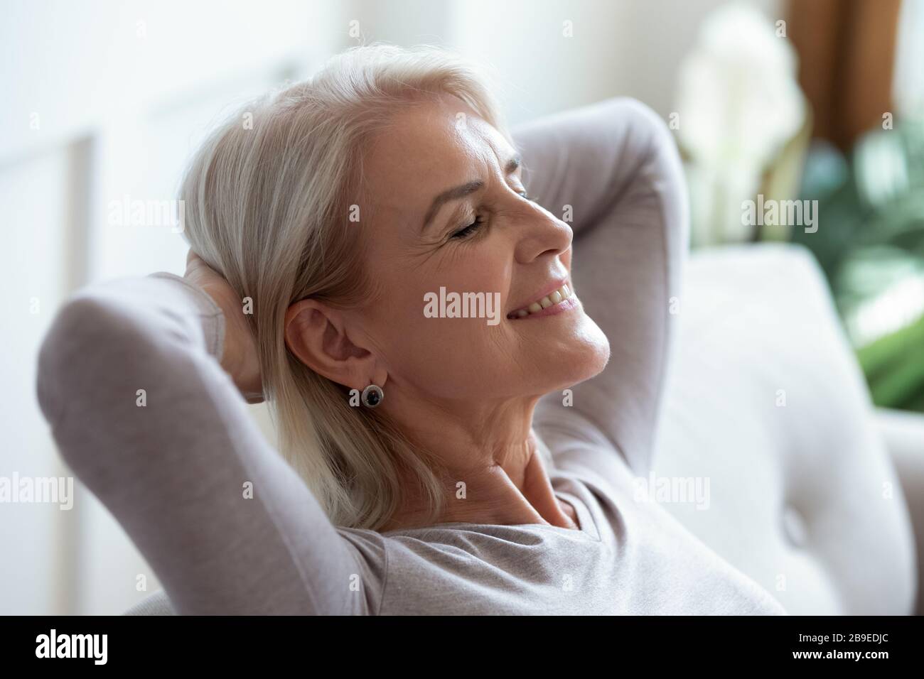 Femme âgée souriante se reposant avec les mains derrière la tête Banque D'Images