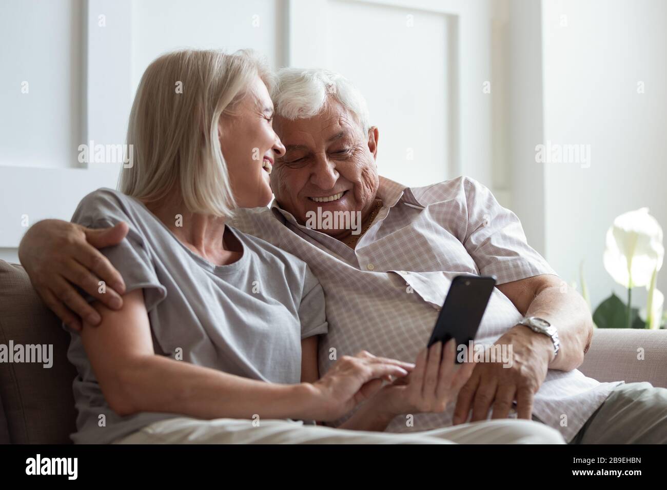 Heureuse femme plus âgée et homme embrassant, en utilisant le téléphone ensemble Banque D'Images
